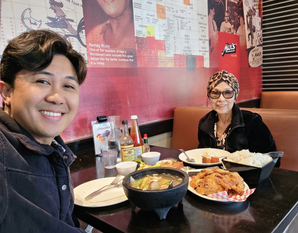 Joël and his mother, Lea, smiling at a table at Max's Restaurant. Lea wears a patterned headscarf.